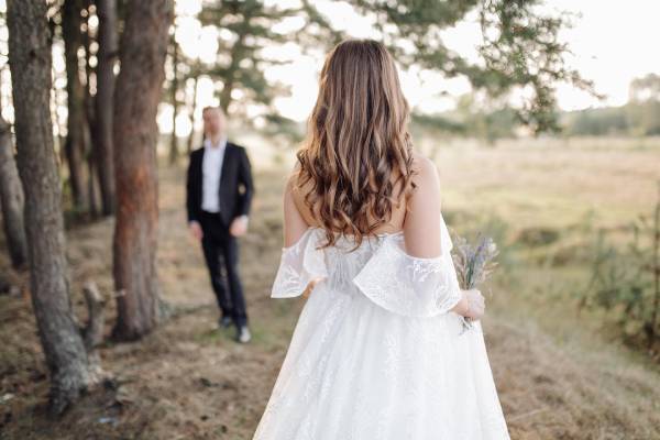 Brudpar på en åker där bruden har ryggen mot bröllopsfotografen och sin brudgum framför sig som inte är i fokus.